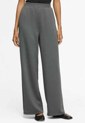 Pantalon gris à jambes larges avec taille élastique, porté avec un haut noir et des chaussures plates noires, montré de la taille aux pieds sur fond blanc.
