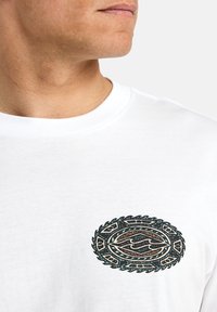 Hvid bomulds-T-shirt med en oval, flerfarvet grafisk design på brystet, med intrikate detaljer og teksturerede accenter.