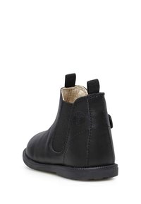 Botín Chelsea de cuero negro con panel lateral elástico y lengüeta. Textura suave, punta redondeada y suela de goma. Diseño minimalista.
