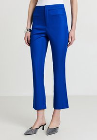 Pantaloni su misura di un brillante blu con vestibilità slim, lunghezza accorciata, frontale piatto e due tasche laterali, abbinati a scarpe con punta nera e argento.