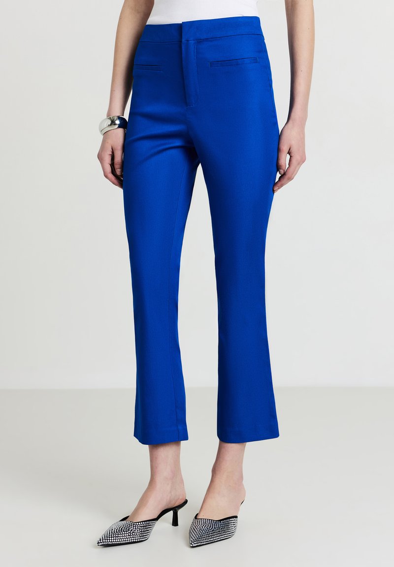 Pantaloni su misura di un brillante blu con vestibilità slim, lunghezza accorciata, frontale piatto e due tasche laterali, abbinati a scarpe con punta nera e argento.