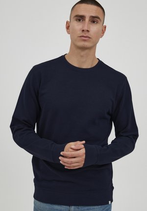 Navy blue long-sleeve sweatshirt in cotton blend with crew neckline and ribbed cuffs. Features a subtle brand tag near the hem.