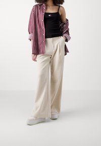 Camicia a righe rossa e bianca sopra una canotta nera. Pantaloni a gamba larga color crema in maglia a coste e scarpe da ginnastica bianche con suola verde.