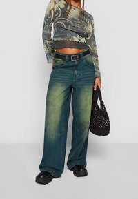 Modré-zelené široké džíny se zesvětlením, černý opasek a masivní černé platformové boty; doplněné o vzorovaný dlouhý rukáv.