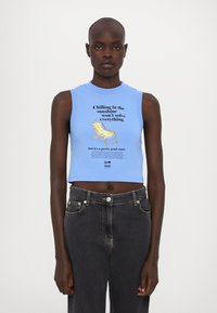 Svetlomodrý bezrukávový crop top s textom a ilustráciou stoličky. Kombinovaný s tmavomodrými rifľovými nohavicami s vysokým pásom. Hladká textúra.