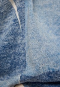 Hellblauer Stoff mit einer leicht strukturierten Oberfläche, der eine Mischung aus helleren und dunkleren Farbtönen zeigt. Weiches, flexibles Material mit subtilen Variationen.