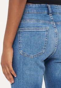Blå denim jeans med høy midje, fem-lommers stil, kontraststing og en baklomme med en triangulær klaff.