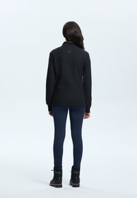 Svart långärmad tröja med krage, tillsammans med marinblå leggings och svarta stövlar. Slät tyg med minimal detaljering på baksidan.
