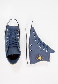 Modré plátěné tenisky s vysokým svrškem, bílou gumovou podrážkou, hvězdným logem na boku a modrými plochými tkaničkami. Mají strukturovaný povrch a kovové průchodky.