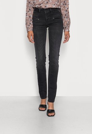 Woman wearing faded black skinny jeans with front zipper pockets, paired with a patterned long-sleeve blouse and black open-toe heeled sandals.
