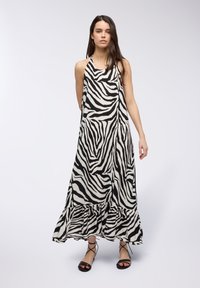 Abito maxi in stampa zebra bianco e nero, design con collo halter, tessuto fluido con orlo arricciato, abbinato a sandali neri.