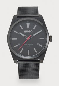 Reloj analógico negro con caja hexagonal, esfera gris, segundero rojo y correa de malla negra. Resistente al agua hasta 5 bares.