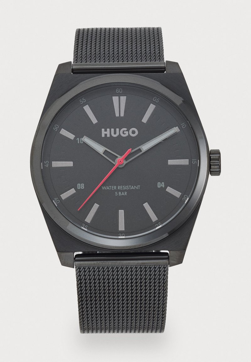 Reloj analógico negro con caja hexagonal, esfera gris, segundero rojo y correa de malla negra. Resistente al agua hasta 5 bares.
