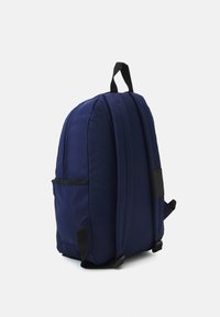 Zaino blu navy con design imbottito, accenti neri, due spallacci e una tasca laterale. Texture liscia e forma arrotondata.