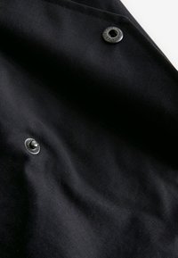 Tissu noir avec deux boutons-pression en métal noir, dont un avec un nom de marque et des chiffres en relief.