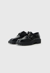 Zapatos de cuero negro con acabado brillante, con un acento de hebilla, suela de goma gruesa y diseño de punta redonda.
