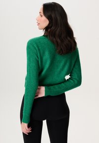 Groene gebreide trui met een geribbelde textuur, lange mouwen en een relaxte pasvorm. Van achteren bekeken, gecombineerd met zwarte leggings.