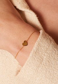 Gouden armband met een delicaten ketting en een kleine, gepolijste hartbedel. De bedel heeft twee kleine gaten voor een veilige bevestiging.