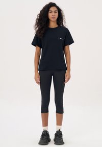 Zwarte katoenen t-shirt met korte mouwen en een klein logo, gecombineerd met zwarte cropped leggings en zwarte sport schoenen. Witte sokken zichtbaar.