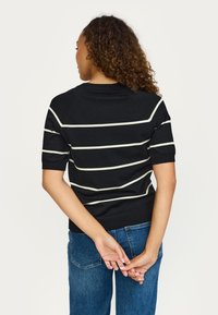 Črni pulover s kratkimi rokavi z belimi vodoravnimi črtami, rebrastimi manšetami in spodnjim robom. Nošen z visokim pasom modrih kavbojk.