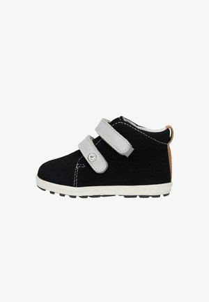 Bottines noires en daim avec des sangles en Velcro grises, semelle blanche, coutures contrastées et un petit accent orange au talon.