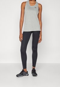 Szary bezrękawnik sportowy, czarne legginsy i czarne buty do treningu. Top ma okrągły dekolt i subtelne logo marki.