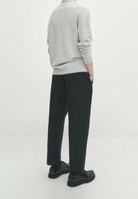 Grijze sweatshirt gecombineerd met zwarte wijde broek en zwarte schoenen. De outfit heeft een relaxte pasvorm en gladde texturen.