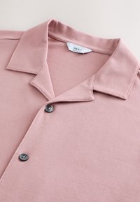 Polo rosa realizzata in tessuto strutturato, con colletto appuntito, due bottoni sulla patta e un'etichetta all'interno del colletto.