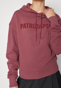 Felpa con cappuccio color bordeaux, con una stampa testurizzata di "PATRIZIA PEPE" sul petto, caratterizzata da polsini e orlo a costine. Tessuto morbido.
