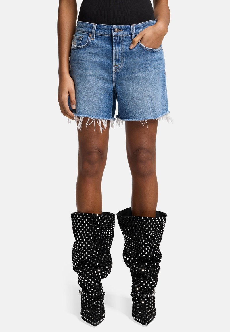 Lichtblauwe denimshorts met rafelige zoom, gecombineerd met zwarte, glanzende kniehoogte laarzen met zilveren stippen en een slouchy ontwerp.