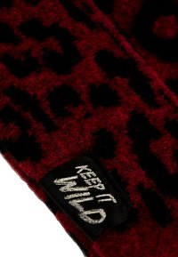 Tela de patrón rojo y negro con una textura peluda. Presenta una etiqueta negra con "MANTENLO SALVAJE" en letras plateadas.