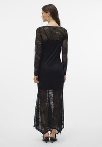 Svart laceklänning med långa ärmar, en figursydd överdel och en utsvängd, genomskinlig kjol. Mönster med textur över hela klänningen och en hög-låg fåll.