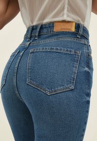 Blauwe spijkerbroek met een hoge taille, voorzien van een leren label, dubbel gestikte zakken en een licht vervaagde textuur.