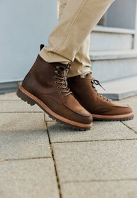 Stivali in pelle marrone con finitura texturizzata, design con lacci, suola in gomma e suola esterna in un marrone chiaro a contrasto. Adatti per l'uso casual.