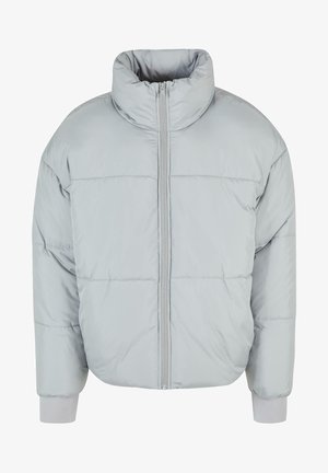 Svetlo siva puhovka z visokim ovratnikom, sprednjim zadrgo in rebrastimi manšetami. Ima šivane panele za teksturo in toploto.