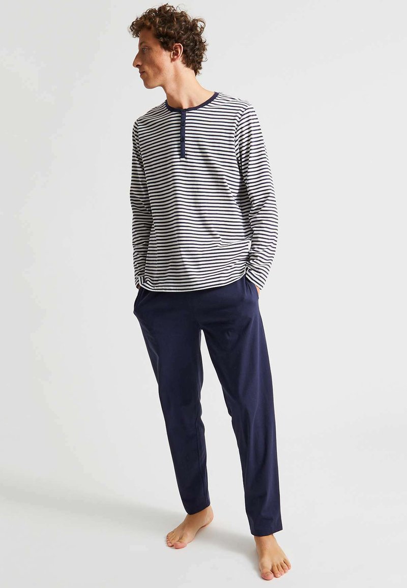 Chemise à rayures à manches longues en blanc et marine, avec un col henley. Associée à un pantalon droit en marine foncé, en tissu léger.