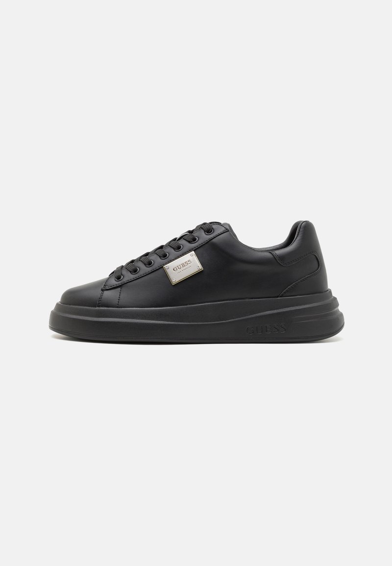 Zapatilla de cuero negro con punta redonda, suela plana y diseño de cordones. Presenta una placa de logo metálica en el lateral y una textura suave.