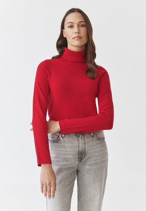 Roter Rollkragenpullover mit langen Ärmeln, aus einem glatten Strickstoff gefertigt. Hat ein tailliertes Design und einen gerippten Kragen, kombiniert mit hochtaillierten Jeans.