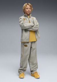 Ensemble de survêtement Puma en gris clair avec des accents jaunes, comprenant une veste zippée et un pantalon ample. Baskets jaunes vives.