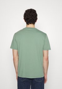 Grön bomullströja med korta ärmar och rundad hals, med en slät yta och enkel design, sedd bakifrån.