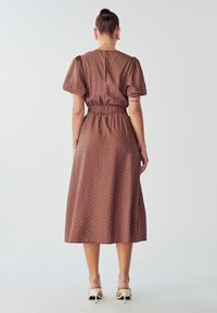 Robe midi marron à pois avec des manches bouffantes, taille élastique et fermeture éclair au dos, présentant une texture lisse et une silhouette fluide.