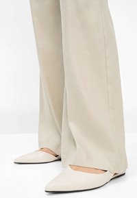 Pantaloni beige a gamba larga realizzati in tessuto liscio con un taglio dritto, abbinati a scarpe basse color crema a punta con un design minimalista.