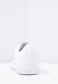 Baskets blanches basses vues de dos sur une surface blanche, avec des coutures visibles et un petit logo sur le talon.
