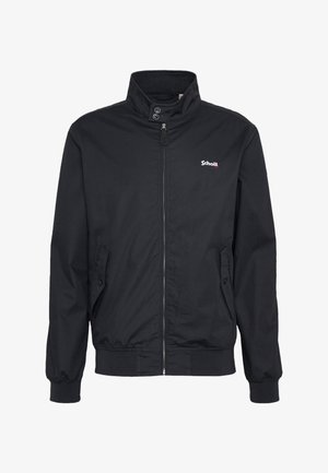 Schwarze Zip-up-Jacke mit hohem Kragen, zwei Knöpfen am Kragen, Vordertaschen mit Knopfverschlüssen und kleinem weißem "Schott"-Logo auf der Brust.