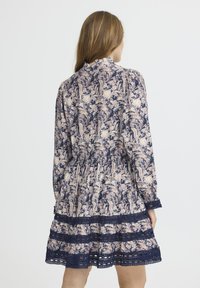 Ziedu motīvu kleita tumši zilā un krēmkrāsā, ar garām piedurknēm, ruffle apvalku, un mežģīņu apdari ap apakšmalu, kā arī savelku vidukļa dizainu.