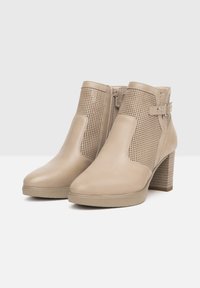Stivaletti beige alla caviglia in pelle liscia con pannelli laterali perforati, tacco a blocco e zip laterale. Il tacco texturizzato aggiunge profondità.