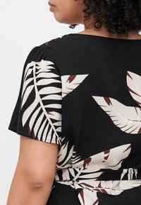 Black dress with short sleeves featuring a large beige and maroon leaf pattern. Smooth fabric texture and relaxed fit, tied at the waist.