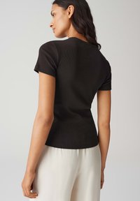 Top in maglia nera a coste con maniche corte, silhouette aderente e scollo rotondo, abbinato a pantaloni fluidi color crema.
