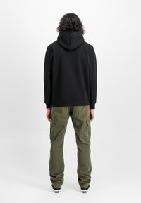 Felpa nera con cappuccio ampio e polsini a coste, abbinata a pantaloni cargo verde oliva con tasche laterali e vestibilità comoda.