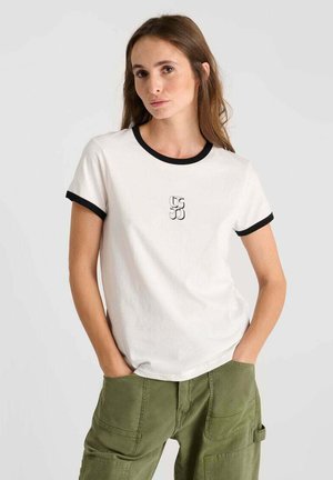 T-shirt blanc à manches courtes avec col et poignets noirs, arborant un logo graphique minimaliste sur la poitrine. Tissu en coton doux.